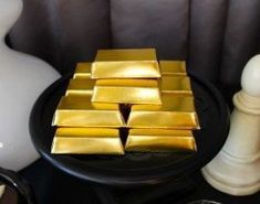 some gold bars sitting on top of a black table next to a white vase and lamp