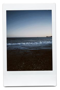 a polaroid photo of the ocean at dusk with waves coming in from the shore