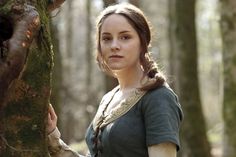 a woman standing next to a tree in the woods