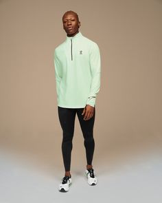 a man standing in front of a gray background wearing a green shirt and black leggings