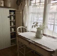 a kitchen table with a vase on top of it next to a white cabinet and window