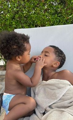 two young children are sitting on a towel and one is touching the other's face