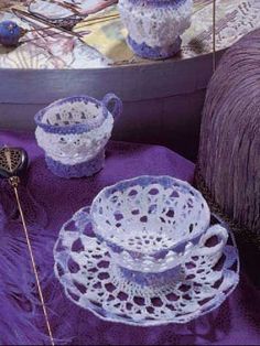 crocheted dishes and cups are sitting on a purple cloth