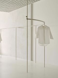 two white shirts hanging on clothes racks in an empty room