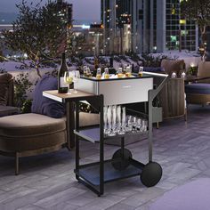 an outdoor bar cart with wine glasses and bottles on it in front of a cityscape