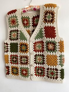 a crocheted vest hanging on a wall with a white hanger attached to it