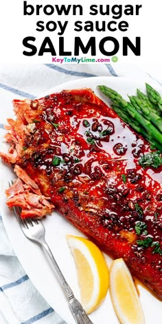 a white plate topped with salmon and asparagus next to lemon wedges on a striped towel