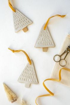 four ceramic christmas trees with yellow ribbon and scissors on a white surface next to other ornaments