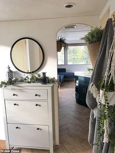 a room with a dresser, mirror and hanging plants on the wall next to it