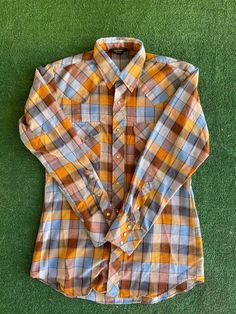 "Vintage 70s blue, orange, and brown with a hint of metallic silver, plaid long-sleeve Western shirt with pearl snaps. Made by Sears. The tag says medium/15-15.5\" Western Wear. Cotton and Polyester blend. Nice comfortable, lightweight material and in fabulous vintage condition. Measurements laying flat Armpit to armpit 21\" (42\" total) From the top of the shoulder to the bottom of the sleeve cuff 30.5\"  Total length of shirt 30\" Items are shipped out within 1-2 business days. If you have any Orange Fall Shirt With Button Closure, Fall Orange Shirt With Button Closure, Brown Shirt With Snap Buttons For Fall, Brown Long Sleeve Shirt With Snap Buttons, Brown Western Style Shirt For Fall, Brown Western Shirt For Fall, Retro Orange Long Sleeve Shirt, Retro Plaid Shirt For Fall, Brown Long Sleeve Flannel Shirt For Spring