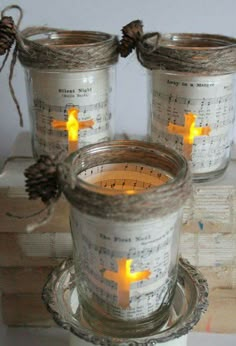 three lit candles in glass jars with sheet music notes and pinecone decorations on them