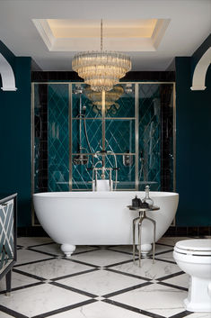 a white bath tub sitting inside of a bathroom next to a toilet and chandelier