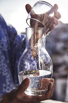 a person is pouring water into a large glass vase with sand in it on the table