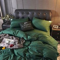 a bed with green sheets and pillows in a bedroom next to a black leather headboard