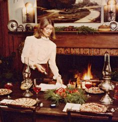 a woman standing in front of a fire place with food on the dining room table