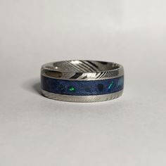 a silver ring with blue and green inlays sits on a white surface,