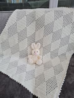 a teddy bear sitting on top of a white crocheted blanket