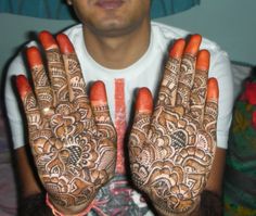 a man is holding his hands with hendi tattoos on their palms and the fingers are painted orange