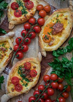 some bread with tomatoes and other toppings on a wooden table next to fresh herbs