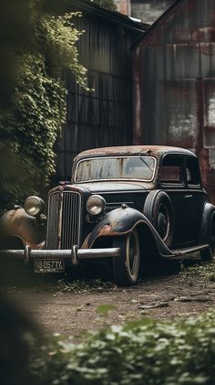 an old car is parked in front of a rusty building with trees and bushes around it