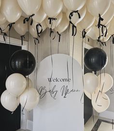 white and black balloons are hanging from the ceiling in front of a welcome baby mama sign