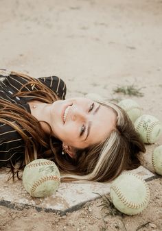 a woman laying on the ground with baseballs in front of her and smiling at the camera