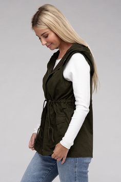 A versatile fashion piece that seamlessly blends style and utility. This vest boasts a convenient zipper and snap-button closure, ensuring ease of wear, while the adjustable drawstring waist provides a personalized, flattering fit. With practical pockets, it's a fashionable yet functional addition to any outfit, making it perfect for both casual and statement looks. Model is wearing a SmallModel SpecsHeight: 5'8"Bust: 34D Waist: 24"Hips: 37"*Color may vary slightly due to monitor resolutionMade Hooded Outdoor Vest For Spring, Sleeveless Cargo Pocket Outerwear For Spring, Casual Outerwear With Drawstring For Outdoor Activities, Casual Sleeveless Outerwear With Cargo Pockets, Khaki Vest With Side Pockets For Fall, Trendy Outdoor Vest For Fall, Casual Fall Vest With Pockets, Fall Cotton Vest With Side Pockets, Hooded Outdoor Vest With Pockets