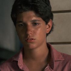 a close up of a person wearing a pink shirt and looking at the camera with a serious look on his face