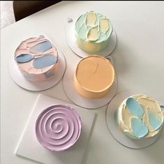 four different colored cakes sitting on plates next to each other with frosting swirls