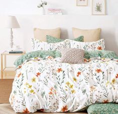 a bed with floral comforter and pillows in a white room next to a lamp