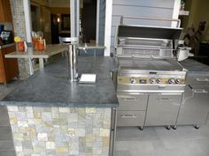 an outdoor kitchen with stainless steel appliances and granite counter tops, along with tile flooring