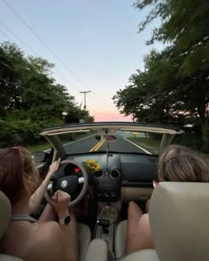 two people sitting in the driver's seat of a car driving down a road