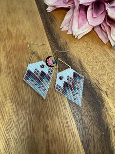 a pair of beaded earrings sitting on top of a wooden table next to pink flowers