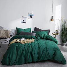 a bed with green comforter and pillows in a white room next to a chair