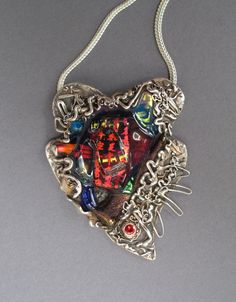 "This beautiful heart shaped pendant with a dichroic cabochon is my original design, created in my studio. The dichroic glass cabochon has iridescent blue, red and gold colors surrounded by free form silver  with a little accent of red CZ on the bottom. I used recycled fine silver to create this romantic and rustic piece. Dichroic glass reflects light beautifully and in combination with silver texture it makes this pendant real art statement. It have been oxidized to bring out the texture with a Unique Iridescent Nickel-free Necklace, Unique Iridescent Cabochon Necklaces, Iridescent Necklace With Large Pendant In Unique Style, Unique Soldered Heart Necklace, Unique Handmade Heart Pendant Jewelry, Unique Heart-shaped Soldered Necklace, Unique Handmade Heart-shaped Jewelry, Handmade Iridescent Pendant Jewelry, Artistic Heart-shaped Sterling Silver Jewelry