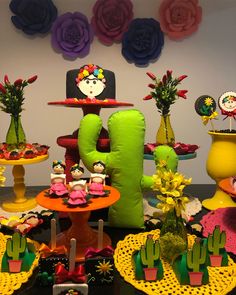 a table topped with lots of cakes and desserts next to colorful paper flowers on the wall