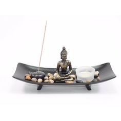 a buddha statue sitting on top of a black tray with rocks and candles in it