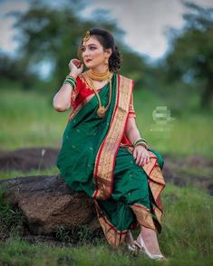 a woman sitting on top of a rock wearing a green and red sari dress