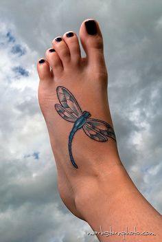 a woman's foot with a dragonfly tattoo on her left leg and the sky in the background