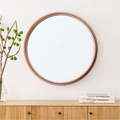 a round mirror sitting on top of a wooden dresser next to a vase filled with flowers