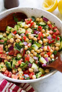 a salad with chickpeas, cucumber and tomatoes in a white bowl