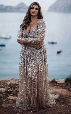 a woman standing on top of a cliff next to the ocean wearing a long dress