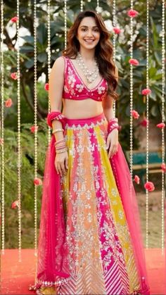 a woman in a pink and yellow lehenga with beads hanging from the ceiling