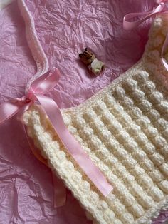 there is a crocheted bag with a pink ribbon on the side and a teddy bear next to it