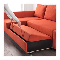 an orange couch with a pull out bed in front of it and a person reaching for something