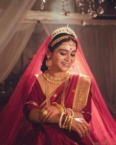 a woman in a red and gold bridal outfit smiles as she sits on the floor