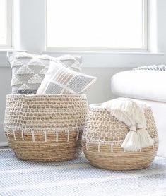 two woven baskets sitting on top of a rug next to a white chair and window