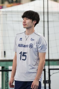 a young man standing in front of a volley ball net with his head turned to the side