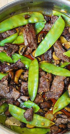 a pan filled with meat and vegetables on top of a wooden table next to utensils