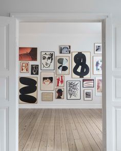 an open door leading to a white room with pictures on the wall and wooden floors